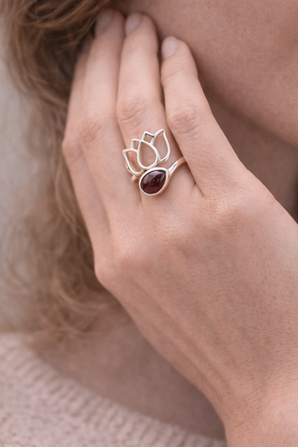 Bague Lotus en argent 925 avec pierre grenat et motif florale délicat, portée sur le doigt près du visage. Amour et vitalité.