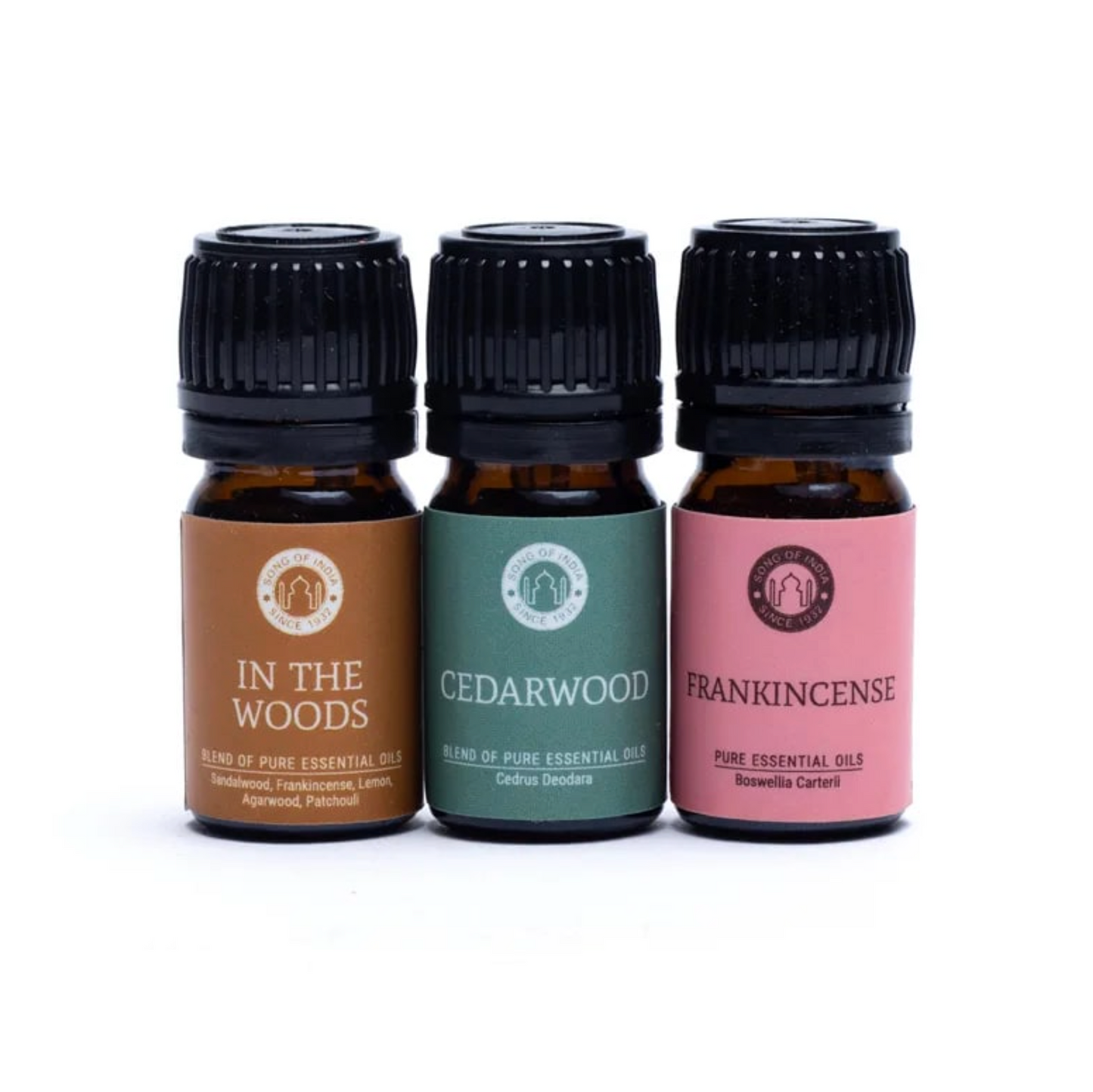 Trois fioles d’huiles essentielles alignées dans des étiquettes colorées (In The Woods, Cedarwood, Frankincense) et bouchons noirs. Coffret Huiles Essentielles Équilibre et relaxation.