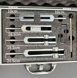 Set de 5 diapasons thérapeutiques avec boîtier contenant pièces métalliques et outils, indiquant mesures 10 cm, 16,5 cm, 18,2 cm et 21,5 cm.