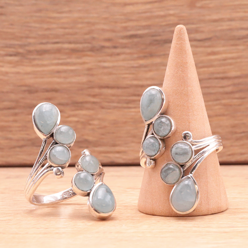 Bague argent 925 et pierre bleue clair, esprit voile de clarté, motifs en gouttes et perles délicates sur foncé bois. Calme et expression.