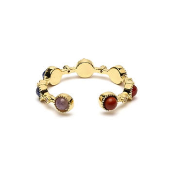 Bague ouverte dorée à motifs circulaires avec sept pierres de chakras colorées sur les extrémités, évoquant l’équilibre énergétique.